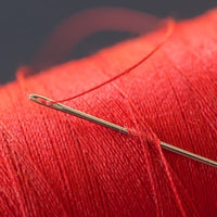 A needle slipped into a spool of red cotton